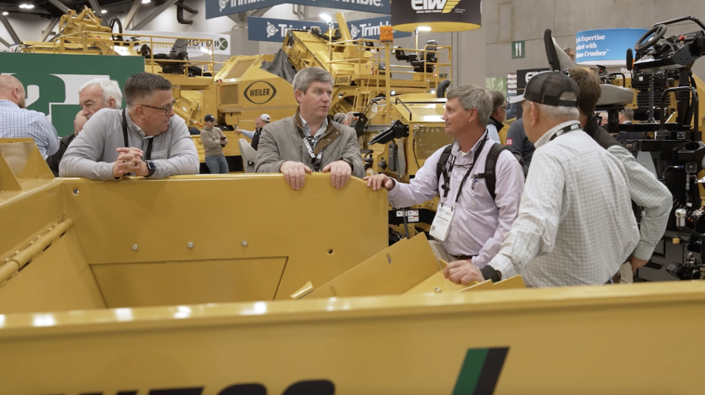 Attendees gather around a machine chatting at the World of Asphalt Conference, hosted by AEM. 